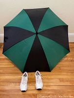 Top view of golf umbrella with alternating green and black panels and white women's Adidas golf shoes in front.