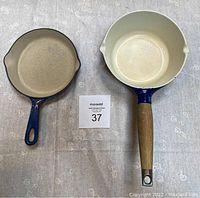 Two enameled cast iron pans: Le Creuset #16 pan and Copco sauce pan side by side on fabric background with lot number in center.