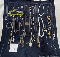 Full view of assorted costume jewelry laid out on dark fabric, showing variety of necklaces, bracelets, earrings, and pins.