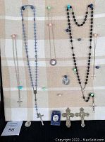 Photo of religious jewelry laid out against a fabric-covered display board showing two rosaries, various cross necklaces, pendants, a medal, and a pin.