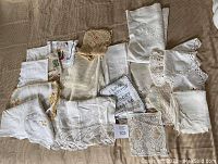 Overview of a collection of vintage linens displayed on a neutral checkered surface showing variety in texture, lace, embroidery, and crochet styles.