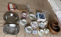 Full lot overview showing 7 china cup and saucer sets, 4 wooden bowls, 2 stainless bowls, 1 creamer, boxed Turkish candleholders, and the outdoor wine glass table.