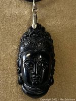 Front view of the carved black stone Buddha head pendant with sterling silver bail against a brown background.