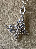 Close-up photo of sterling silver butterfly pendant showing filigree wing design and loop attaching it to chain.
