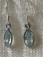 Front view of the pair of sterling silver dangle earrings with marquise-shaped faceted blue topaz stones, showing their icy light blue color and silver settings.