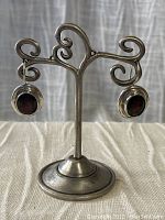 Pair of garnet earrings displayed on a decorative silver stand against a neutral background.