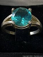 Front view of sterling silver ring with round blue cubic zirconia stone in 4-prong setting on black velvet display.