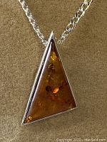 Close-up of triangular amber pendant set in sterling silver on chain, showing warm amber hues and transparency.