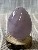 Amethyst carved egg on small rustic wooden stand with reflective and slightly irregular surface.