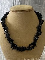 Full view of black onyx gemstone necklace displayed on a tan jewelry bust, showing the black chip beads and round beads.