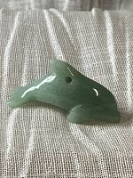 Close-up of polished green jade dolphin figurine showing carved details and hole for hanging.