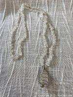 Full view of clear quartz chip necklace arranged on fabric background, showing beads and metal cage pendant