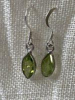 Front view of the pair of faceted peridot sterling silver dangle earrings hung on a white textured background, showing facets and color tone of the stones.