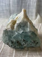 Front view of the natural fluorite crystal showing pale greenish-blue cubic formations with a white crust and dark inclusions at the base.
