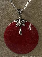 Photo showing the pendant's front with the silver dragonfly bale atop the red round fossil pendant with visible fossil patterns.