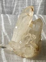 Himalayan quartz crystal cluster showing multiple clear prismatic points with mineral deposits and translucency, resting on a textured fabric background.