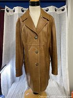 Full front view of the ladies brown leather coat on a mannequin against a curtain background.