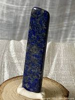 Full view of the polished lapis lazuli slice showing its elongated rectangular shape and polished surface standing upright on a white base in front of a neutral gray background