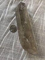 Side view of the large smoky quartz crystal point with a coin placed beside it for scale.