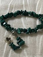 Malachite stone chip bracelet with pierced earrings laid on fabric backdrop showing bracelet circular shape and earring details.