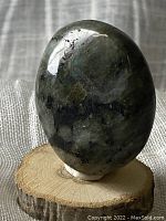 Polished oval labradorite stone on wooden stand, showing smooth texture and sheen.