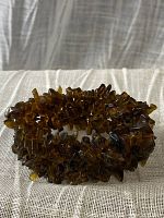 Bracelet laid coiled on a cream fabric surface, showing its dark smoky brown translucent gemstone chips strung tightly together forming a stretchy band.
