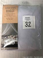 Photo of white polyester mosquito net folded inside clear plastic packaging showing front label with brand Stefania, product type 'Mosquito Net', dimensions 60 x 250 x 1000 cm (24 x 98 x 394 in).
