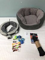 Cat bed with plush interior, cat tunnel, kicker toy and various cat balls and fish toys arranged on a surface
