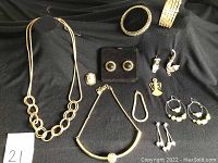 View of all 12 pieces of costume jewellery laid out on black fabric background including necklaces, bracelets, earrings, and ring/brooch.