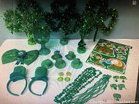 Photo of assorted St. Patrick's Day decorations including garlands, hats, bowties, necklaces, pins, and window decals on a white table against a white background.