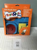 Front view of sealed box packaging for Toys R Us Pets Treat Puzzle Game for dogs; orange background with blue puzzle toy visible through plastic window.