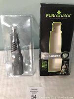 FURminator nail grinder in clear plastic container displayed next to its black and green retail box showing product image and branding.