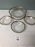 Full view of the set with large bowl and three smaller bowls arranged on a white cloth, showing the hammered gold rims and textured glass.