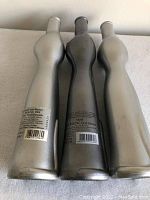 Rear view of three metallic cat-shaped wine bottles showing labels and two light gray, one darker gray color.