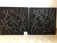 Photo showing two square metal abstract wall art pieces hanging side by side on a white wall, each 24x24 inches, with silver curved rods on black textured backgrounds.