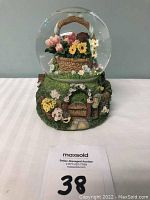 Full view of the snow globe showing clear glass globe on a cottage-inspired base with flowers and door details.