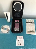 Lot items arranged on blue cloth background including hair removal device, case, cream, manual and CD.