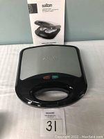 Front and top view of Salton stainless steel waffle maker showing the brand logo, black handle, and indicator lights on front.