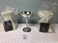 Three handcrafted silver goblets: two sealed in plastic bags and one unpackaged with minor tarnishing, all identical in design and size.