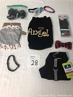 Lot items arranged on a surface showing dog outfits, collars, boots, and accessories including a black rhinestone harness, 'Angel' hoodie, plaid bow tie collar, and other small dog accessories.