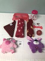 Lot array of dog items: two plush squeaky toys, two mini fleece blankets, checkered bandana, dual-section pet bowl, dental bone, and treat jar.