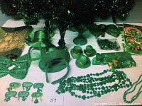 Photo showing various green St. Patrick's Day themed decorations on white surface including hats, bowties, bead necklaces, shamrock window decals, pins, and lace table runner.