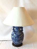 Front view of the Asian blue and white porcelain lamp with cream fabric shade, showing the dragon motifs and overall design.