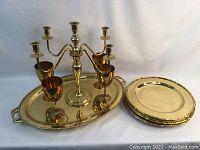Photo showing the brass candelabra, four wine goblets, large platter, and eight charger plates arranged on a white background.
