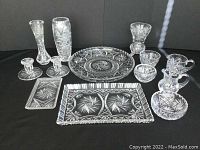 Full lot of assorted pinwheel crystal items including serving trays, candle holders, vases, and cream and sugar set photographed on a black backdrop.