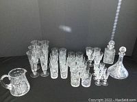 Full lot display showing array of glasses, two different shaped decanters with stoppers, and a crystal water pitcher on black background.