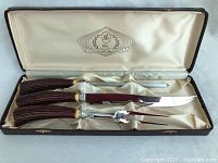 Top-down view of the three-piece carving set in the open lined case, showing knife, fork, and sharpening steel with antler-style handles.