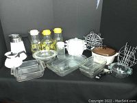 Full overview of all items in lot including Corning Ware cookware, Pyrex glass baking dishes, glass juice bottles, white coffee pots, metal trivets, and a crock pot.
