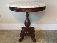 White marble top wooden side table showing full piece from front with decorative carved rose and pedestal base.