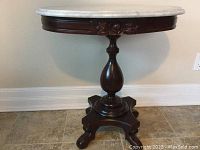 Full view of round wooden side table with white marble top, central pedestal base and carved rose on apron.